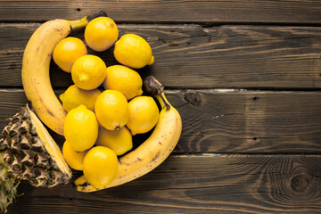 Yellow fruits. Pineapple, bananas and lemons on a wooden background.