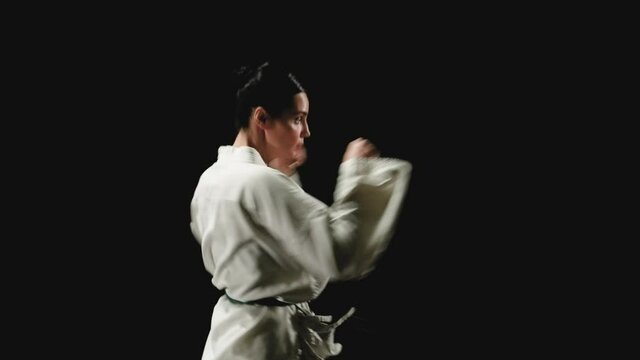 Young woman in kimono practicing karate kicks on a black background. Slow motion