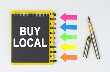 On a white background lies a pen, arrows and a notebook with the inscription - BUY LOCAL