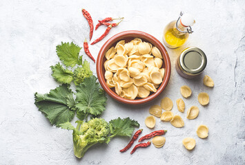 Fototapeta na wymiar Italian handmade pasta Orecchiette with turnip leaves and tops or cima di rapa with salt anchovies, chili pepper, olive oil on white table. Recipes and ingredients of southern Italy, Puglia, Bari