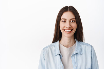 Close up face of young woman with no makeup, nude facial skin and white perfect smile, looking happy at camera, standing in casual clothes