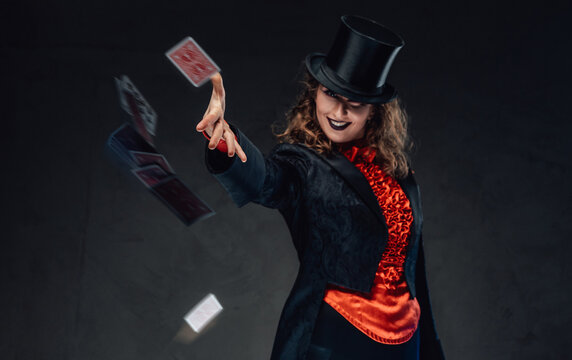 Smiling tricky woman with top hat throws cards in dark background
