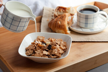 Healthy breakfast in bed served tray in bed with cornflakes and dried fruits and a cup of coffee with croissant. Good start to the day to have the right meal.