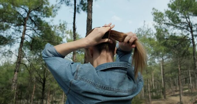 Caucasian woman making ponytail outdoors in the forest.