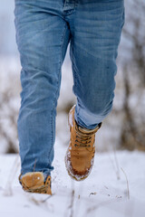 Winter men's shoes made of brown leather. Man walking on snow close up.