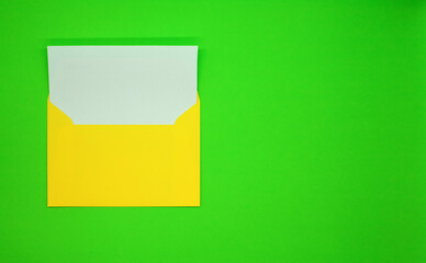 One yellow envelope with a blank white card. Green background.  Mockup with envelope and blank card. Space for text.