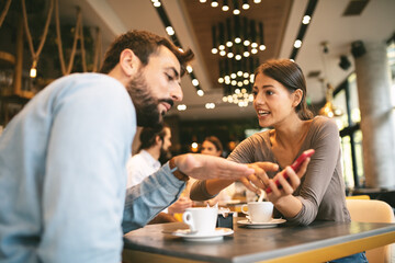 Young happy couple using smartphone in cafe