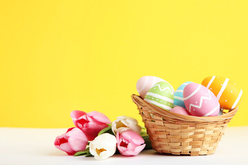 Easter eggs in basket with tulip flowers on yellow background