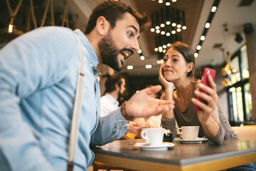 Young happy couple using smartphone in cafe