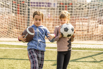 Kids play football on outdoor field. Children score a goal at soccer game. Girls kicking ball. Running child in team jersey and cleats. School football club. Sports training for young player.