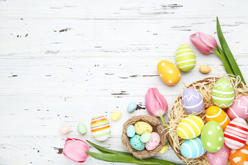 Colorful easter eggs with tulip flowers on white wooden background