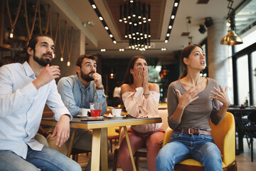 Group of young people watching bad news on tv in a cafe
