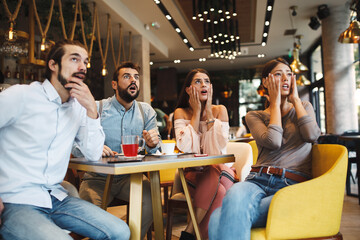 Group of young people watching bad news on tv in a cafe