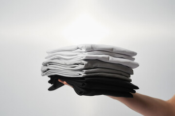 Basic outfit. Male hand holding stack of multi colored t-shirts against grey background - Powered by Adobe