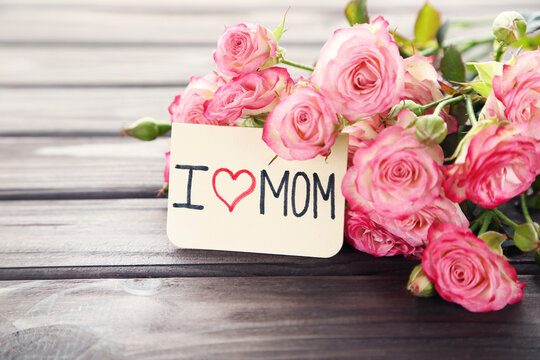 Text I Love MOM with rose flowers on wooden background