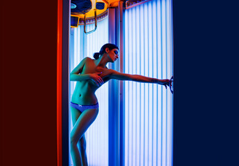 Young sexy woman with tan naked healthy body standing in solarium spa salon. Attractive young girl...