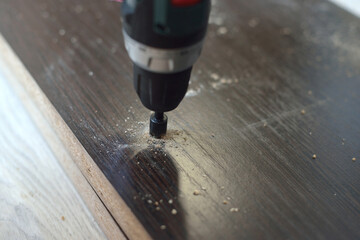 In purple, a man drills a hole in a blank for laminating MDF furniture. MDF furniture assembly concept