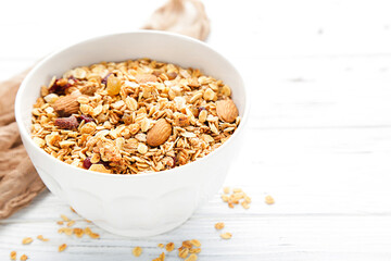 Tasty granola in bowl on white wooden background