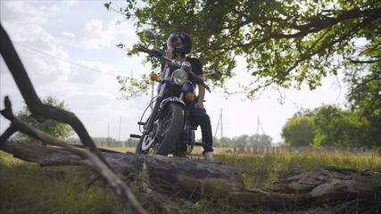 A man on a motorbike against the sea. Motorcyclist stands under a tree. Motorcyclist with a motorcycle in the summer in a clearing.