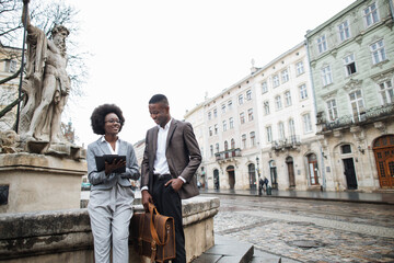 Group of two afro american partners in formal clothes smiling and talking near old fountain on street. Concept of team and partnership.