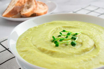 Close up view of classic french chilled cream soup vichyssoise - potato leek soup topped with microgreens in white bowl on marble table background and bread. Healthy food concept. Selective focus