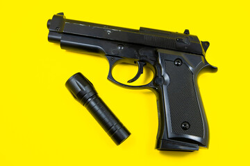 Black gun and flashlight lies on a yellow background. Private detectives work. Searching information concept.