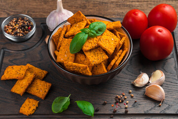 A plate of tomato and garlic crackers with sea salt and basil on a brown background. Side view, close-up.