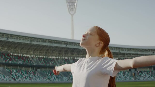 Portrait of Caucasian white girl walking onto the field of huge soccer football stadium, spreading hands, dreaming of becoming professional player, soccer star. Women sport concept