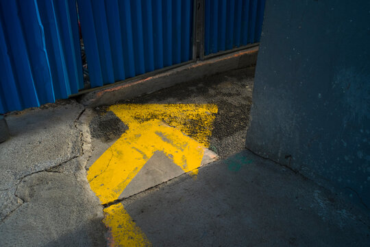 Une fl&egrave;che jaune est peinte sur le sol. Une barri&egrave;re bleue d&eacute;limite le passage dans la direction donn&eacute;e par la fl&egrave;che. Symbole de travaux de voiries dans les rues  pour les pi&eacute;tons