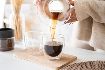 Young woman brewing coffee in coffee pot, pouring coffee to the glass