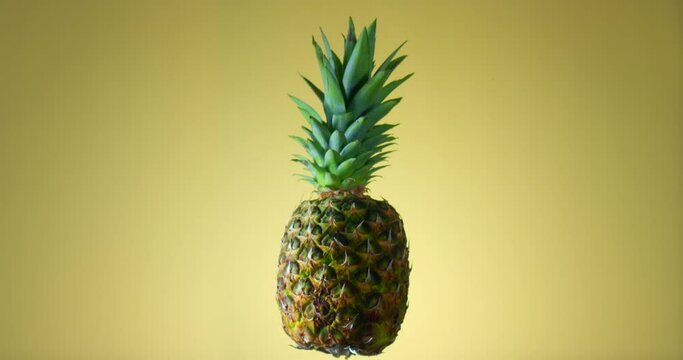 Fresh juicy pineapple rotating on yellow background. Filmed in slow motion with RED camera.