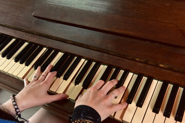 Hands of girl playing classical music on upright piano.