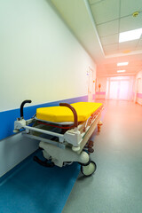 Yellow hospital bed on wheels in wide long modern hall in hospital.