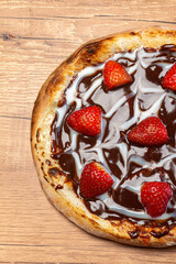 Chocolate pizza with strawberry and sour cream sauce served on a wooden table. Top view. Selective focus.