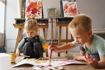 Small children sit on floor and paint with paints