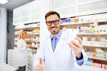 Portrait of smiling caucasian pharmacist holding vitamins in drug store.