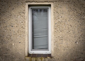 A shabby old window in an ugly house wall with broken lockouts