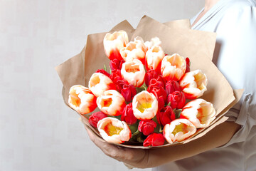 Bright red tulips wrapped in brown paper in female hands. A large bouquet of fresh cut spring flowers. Copy space. A romantic gift for the holiday.