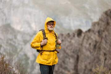 Middle age man traveler in raincoat and backpack enjoying view of mountains.