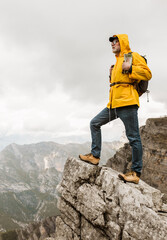 Middle age man traveler in raincoat and backpack enjoying view of mountains.