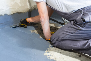 A builder worker applies a waterproofing mortar to the floor in a room.