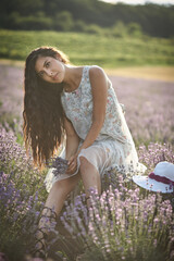 Beautiful girl in a white sarafan sits on a wooden chair and poses in the middle of a lavender...