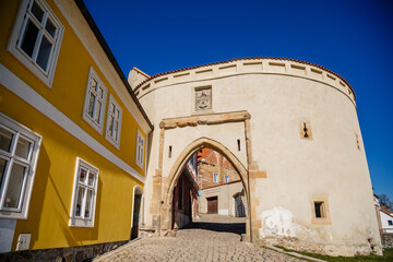 Fototapeta na wymiar Zatecky Barbican, Medieval gothic fortification, fortress wall, sunny day, town gate, old stronghold, city coat of arms, renaissance yellow historical building, Kadan, Czech Republic