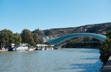 Morning on Kura river or Mtkvari river of Tbilisi, Georgia. The glass bridge or Bridge of Peace and mountain on background. Side view.