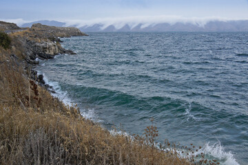 Fototapeta na wymiar Clouds cascade down the hills surrounding Lake Sevan in Armenia on a very windy day in autumn