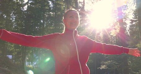 Young woman enjoys at beautiful sunset in pine forest mountain, slow motion, closeup of happy woman spreads her arms and bright sun, branches of the pine trees, season travel nature idyllic