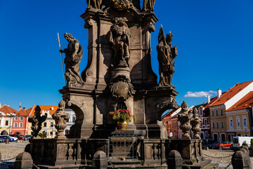 Holy Trinity Column with baroque sculptural group, Main town Peace square, Medieval narrow street, gothic and renaissance historical buildings, sunny day, Kadan, Czech Republic