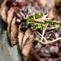 Cutting meat with microgreens. Juicy meat low fat steak sprinkled with herb. Super close up shot. Soft focus. Square format.