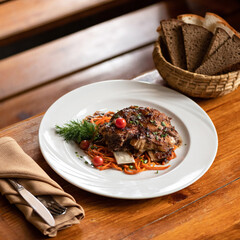 Portion of baked juicy pork ribs with vegetable side dish on plate. Hearty meat lunch served on rustic wooden table with basket of dark bread and cutlery on it. Soft focus. Square format for banner.