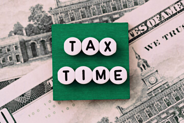 Photo on tax time theme. The inscription "Tax time" on a green square, on the background of dollar bills